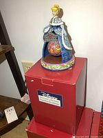 Photo showing full figurine standing on top of its original red Disney Showcase Collections box.
