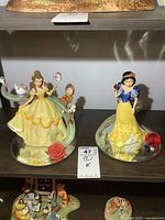 Photo showing both Snow White and Belle figurines on a shelf, with a price tag label visible.