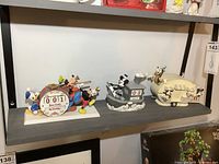 Wide view of three Disney perpetual calendars on shelf showing marching band with musical instruments and drum calendar, Steamboat Mickey boat calendar, and a trailer with Disney characters.