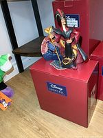 Photo of the Jafar figure standing on its original box, showing front and partial side, on a wooden floor.