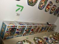 Row of 12 Disney Funko Pop figures, mostly boxed, arranged on a surface under a wall with Disney-themed plaques.