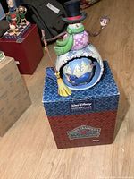 Front view of Disney snowman figurine atop original Disney Traditions box on floor.