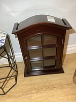 Front view of the wooden display cabinet showing the curved top, glass door with divided panes and a metal knob lock.