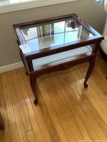 Full view of wooden display table with glass top and sides, showing carved legs and polished wood surface.