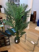 Full view of the tall artificial fern plant in ceramic pot, showing multiple green leaves and wooden floor background.