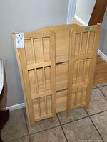 Folded bookshelf front view showing wood panel design with rectangular inset patterns and a sticker label attached on top left corner.