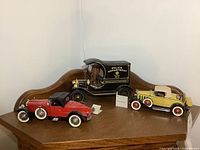 Three Franklin Mint die cast classic car models displayed on a wooden cabinet top: black vintage police car, yellow and tan coupe, red convertible.