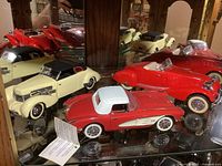Three die cast Franklin Mint classic cars displayed in a glass shelf, showing side and front views.