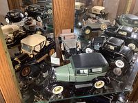 Photo showing four Franklin Mint die cast classic model cars on glass shelf with mirror background