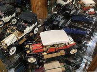 Three Franklin Mint die cast model classic cars displayed on a glass shelf. Front car is a red and black 1910 Rolls-Royce Silver Ghost model with white fabric roof, brass accents, and detailed wheels.