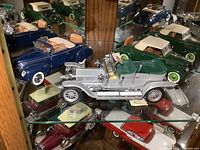 Three Franklin Mint die cast car models displayed on glass shelf. Detailed view of silver vintage convertible with green interior and wood steering wheel.