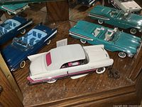 Photo showing two turquoise Ford Thunderbird convertible model cars with detailed blue interiors and one white and pink coupe on a wooden shelf.