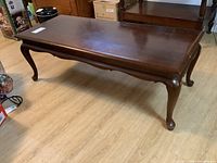 Front and side view of cherry wood coffee table showing Queen Anne style legs and rectangular top with scuffs.