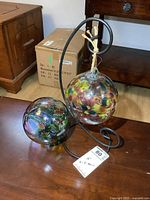 Front view of two multicolored glass balls held within a black curved metal frame placed on a wooden table.