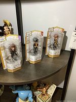 Three Harry Potter Magical Minis figures in original sealed packaging on a curved dark wood surface, including Hermione Granger and two other characters.