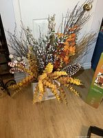 Wide view showing box of assorted artificial decor including twigs, pussy willows, yellow and orange leaves, pine cone, and candy canes.