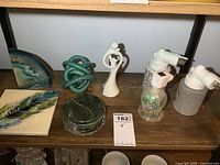 View showing all items on wooden shelf, including coasters, art glass pieces, porcelain figure, decorative tile, and night lights