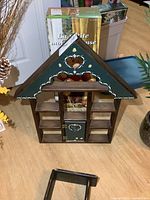 Front view of the wooden house-shaped display shelf with small compartments and decorative painted details.