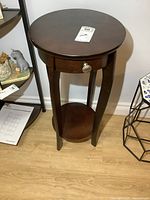 Front view of round wooden lamp table showing drawer knob and lower shelf