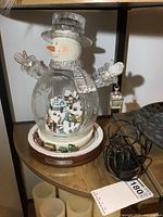 Front view of the light up snowman figurine with train and power cord on shelf