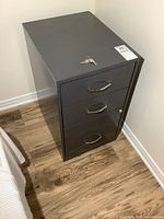 Angled view of the metal file cabinet showing three drawers and keys on top.