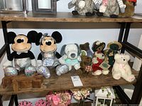 Photo of shelf with two large Disney Mickey and Minnie Mouse plush toys with shiny silver clothing and feet, five smaller bear plush toys including one white bear with a pink bow, one small dog plush, and a wooden puzzle.