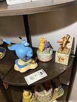 Full view of three Disney musical figures placed on a dark wood shelf; Genie, Pooh & Eeyore, Tigger