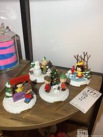 Four Hawthorne Village Peanuts character displays arranged on a shelf, showing all four figurines in various winter poses with a snowy base.