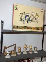 Seven Peanuts nativity figurines displayed on a shelf alongside the nativity stable and original box above them.