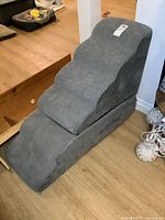 Soft stepped pet ramp with three inclined steps covered in gray fabric with a zippered cover, set on a wood floor near stairs.