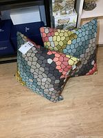Pair of 18-inch square throw cushions with mosaic tile pattern resting on wooden floor, showing front and side views.