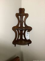 Front view of small wooden corner wall shelf with decorative cut-outs and three shelves.