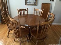 Full view of oval pine dining table surrounded by 6 pine chairs on hardwood floor.