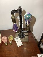 Clear side view of the steampunk lamp showing the two wired bulbs with iridescent finishes and the black iron pipe construction on a wooden base.