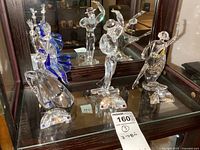 Three figurines displayed on mirrored surface: blue-skirted female, top-hat male, yellow-skirted female.