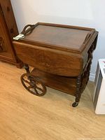 Side view of vintage wooden tea wagon with drop leaf sides down, showing large decorative wheels and small caster wheels.
