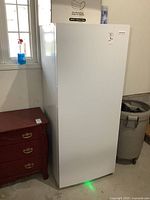 Front view of white Frigidaire upright freezer standing on garage floor.