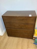 Front view of vintage wooden dresser with 4 drawers showing minor scuffs and wear on surface.