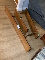 Three solid pine wooden shelves of varying lengths with attached triangular wooden wall brackets, placed on a wood floor.