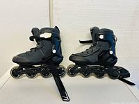 Pair of black adjustable inline roller skates shown side by side on white background, highlighting mesh and plastic boot design with four wheels each.
