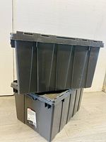 Two black plastic storage totes stacked, showing size and shape.