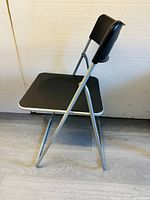 Side view of foldable chair showing black plastic seat and backrest with gray metal frame.