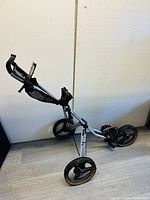 Full view of golf cart showing three large wheels and handle with storage compartment and scorecard holder.