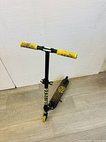 Photo of black kids scooter with yellow handlebar grips, yellow wheels, and black deck showing wear and dirt