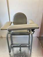 Front view of Lab X Series blood drawing chair, showing padded armrests, rounded padded back, and adjustable foot leveler on metal frame.