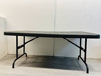Front view of large black foldable table showing rectangular top and metal legs with curved feet.