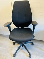 Front view of black ergonomic office chair showing cushioned seat, mesh backrest, and adjustable armrests.