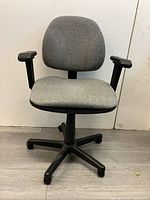 Front view of lightly used gray fabric office chair with black armrests and caster wheel base.
