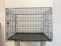 Front top-down view of collapsed or folded metal wire pet cage with plastic bottom tray, showing grid construction and locking door.