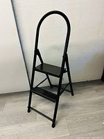 Front view of small black metal 2-step ladder with curved safety handle